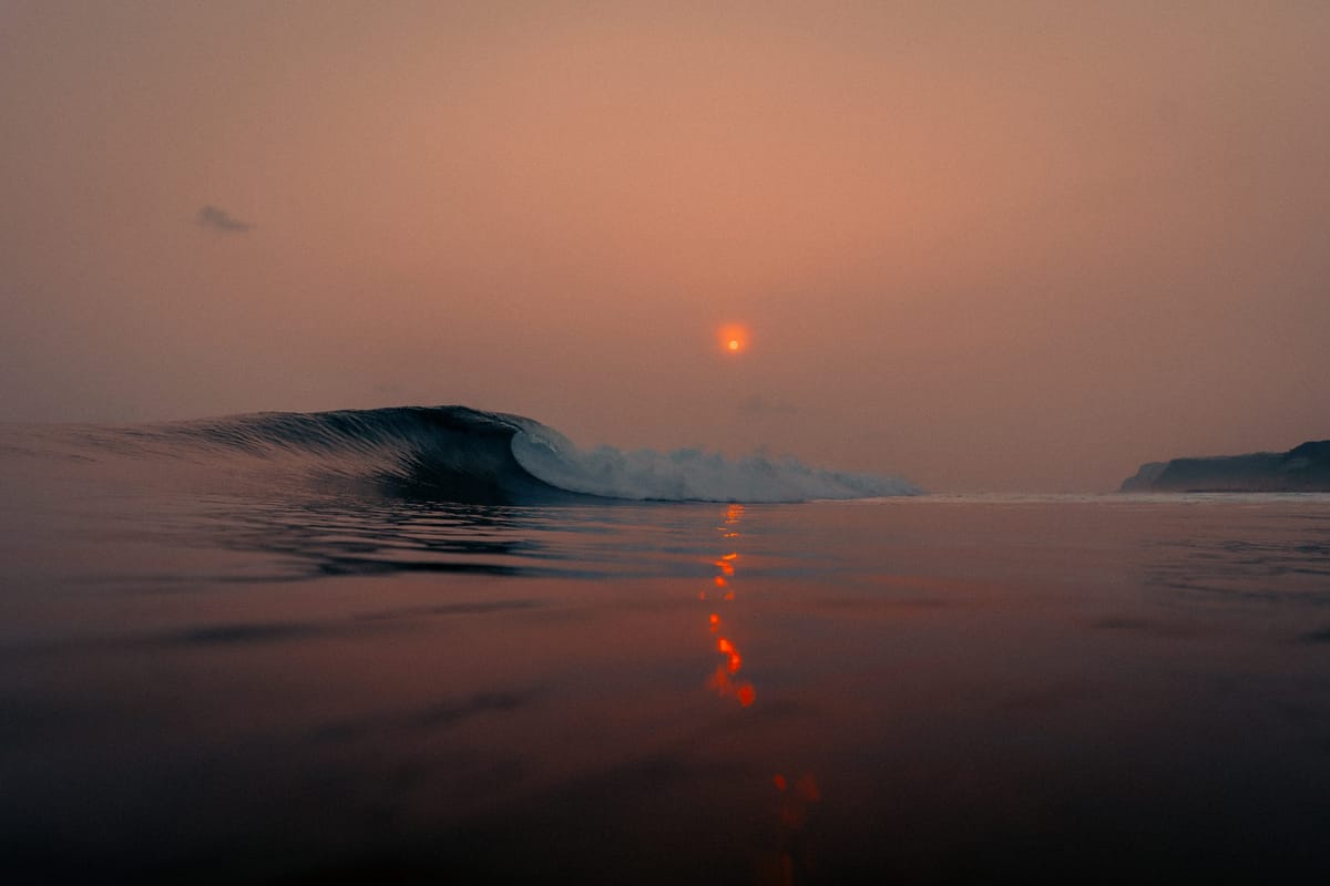 Red sunset over a calm sea, a wave in the distance
